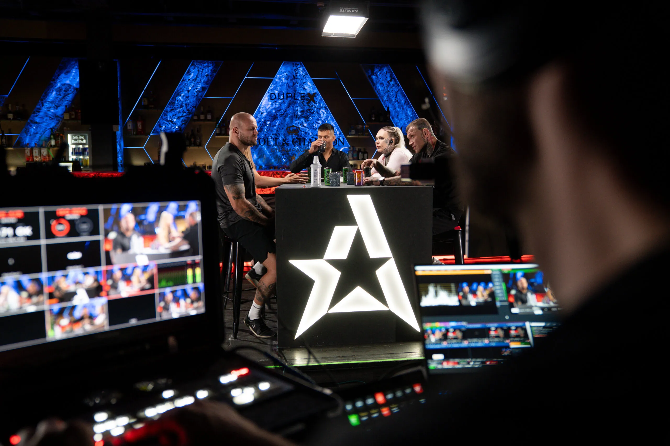 Live broadcast control: multiview monitors, a vision mixer and fighters at the table during a CLASH MMA press conference
