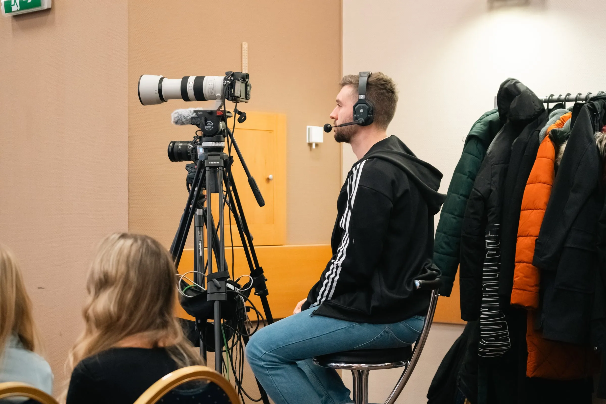Kameraman se sluchátky u kamery na stativu v zadní části konferenčního sálu