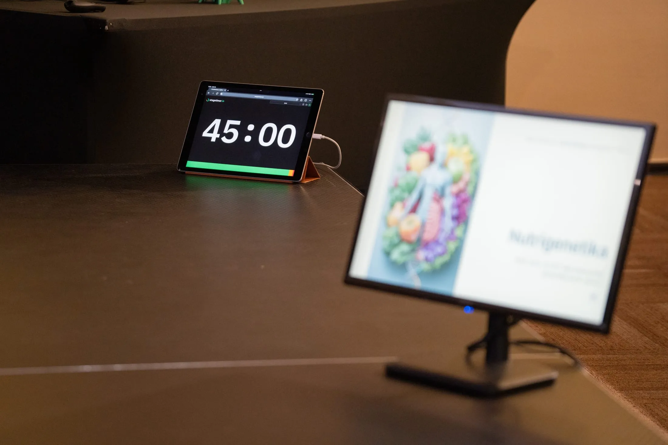 Tablet odpočítava 45 minút na kraji pódia, vedľa neho kontrolný monitor s prezentáciou