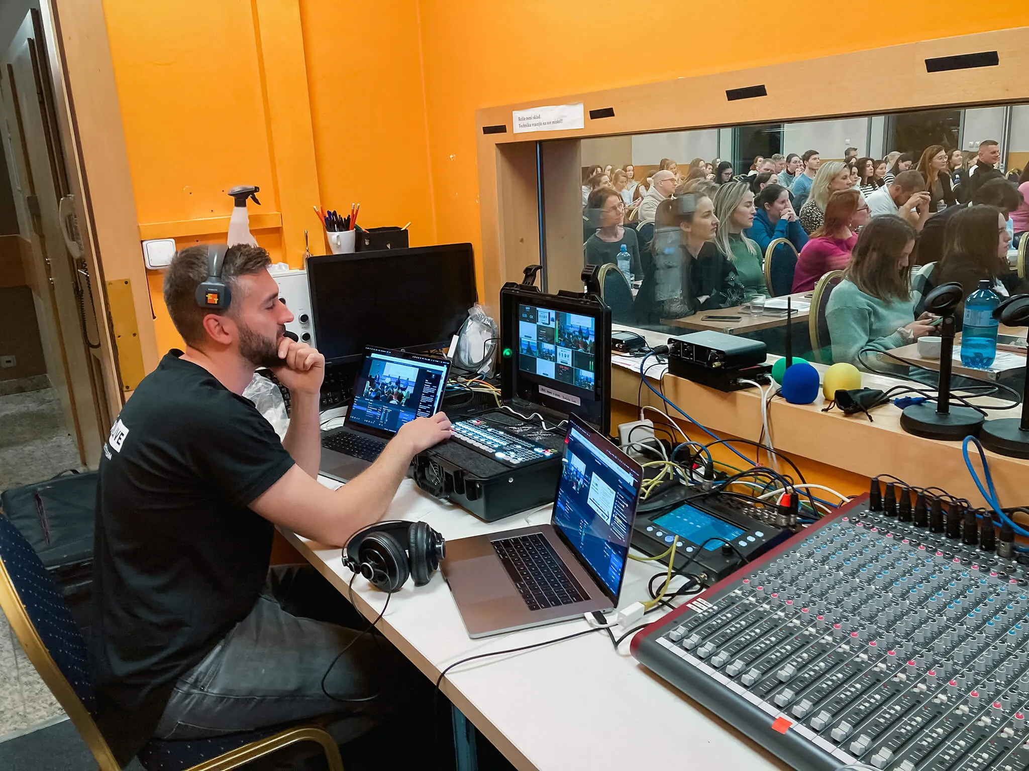 Režisér u mixážního pultu během živého přenosu konference, v pozadí zaplněný sál