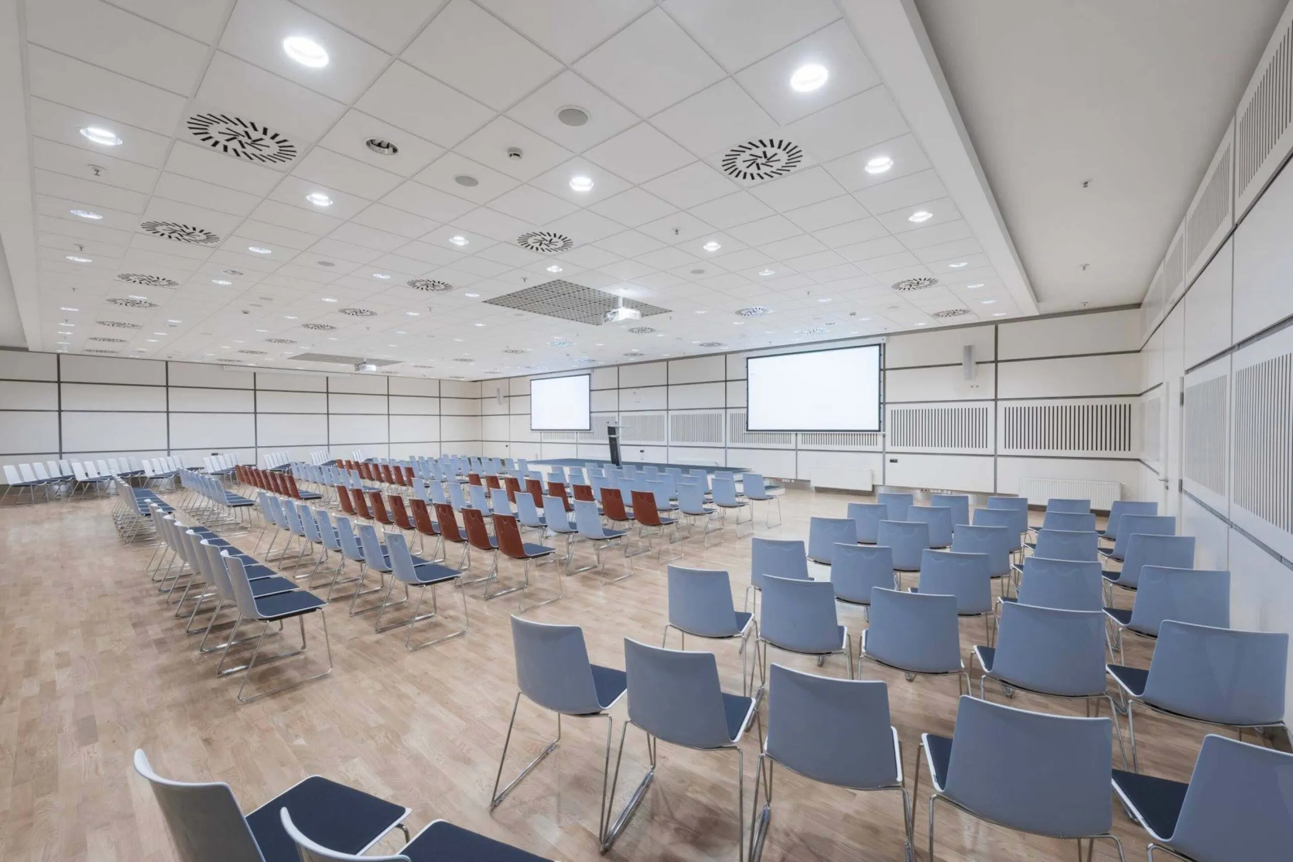 The City Conference Centre lecture room with two screens and rows of blue chairs